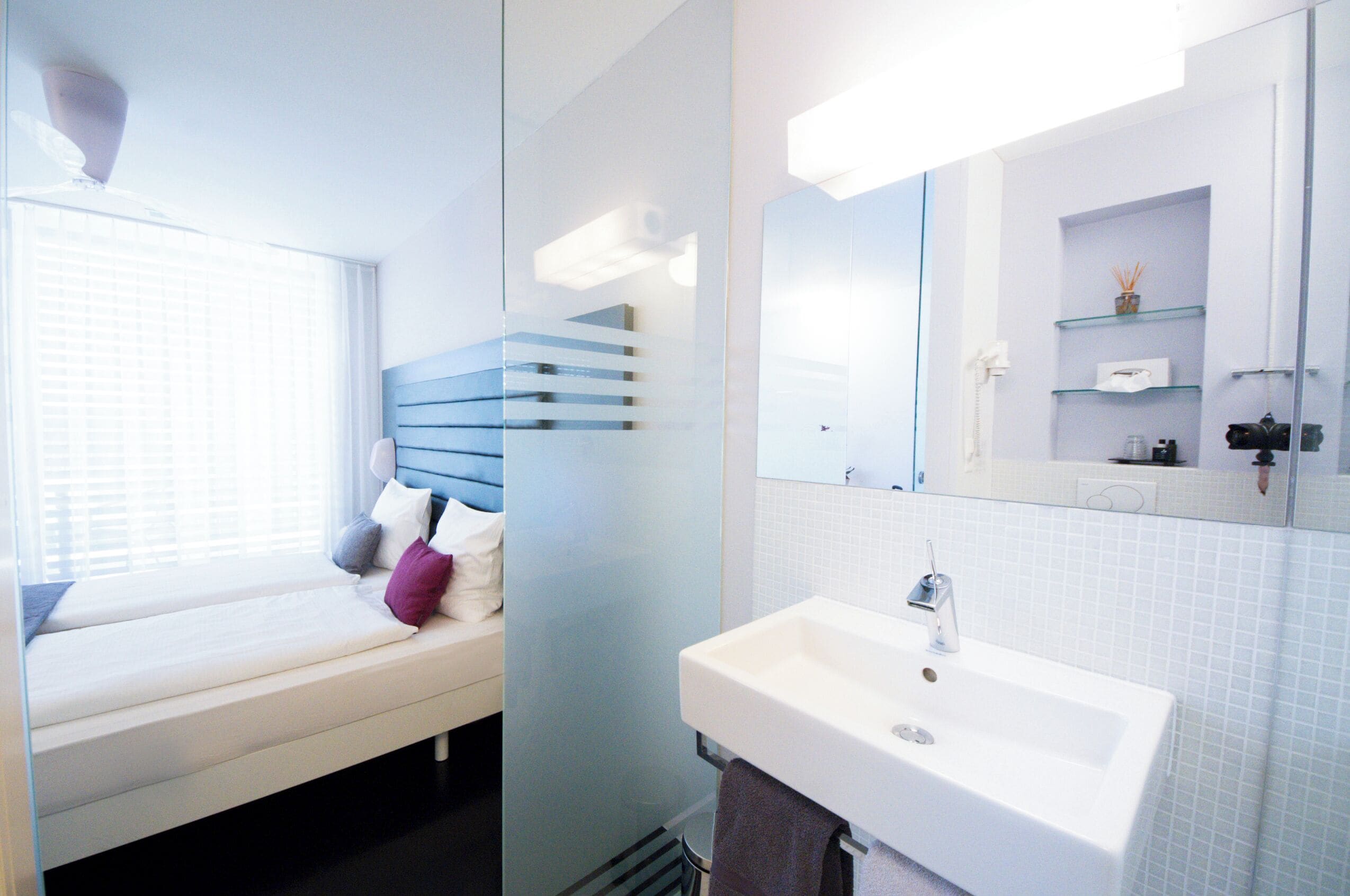 A modern bathroom with a large mirror, a white sink, and a window with blinds.