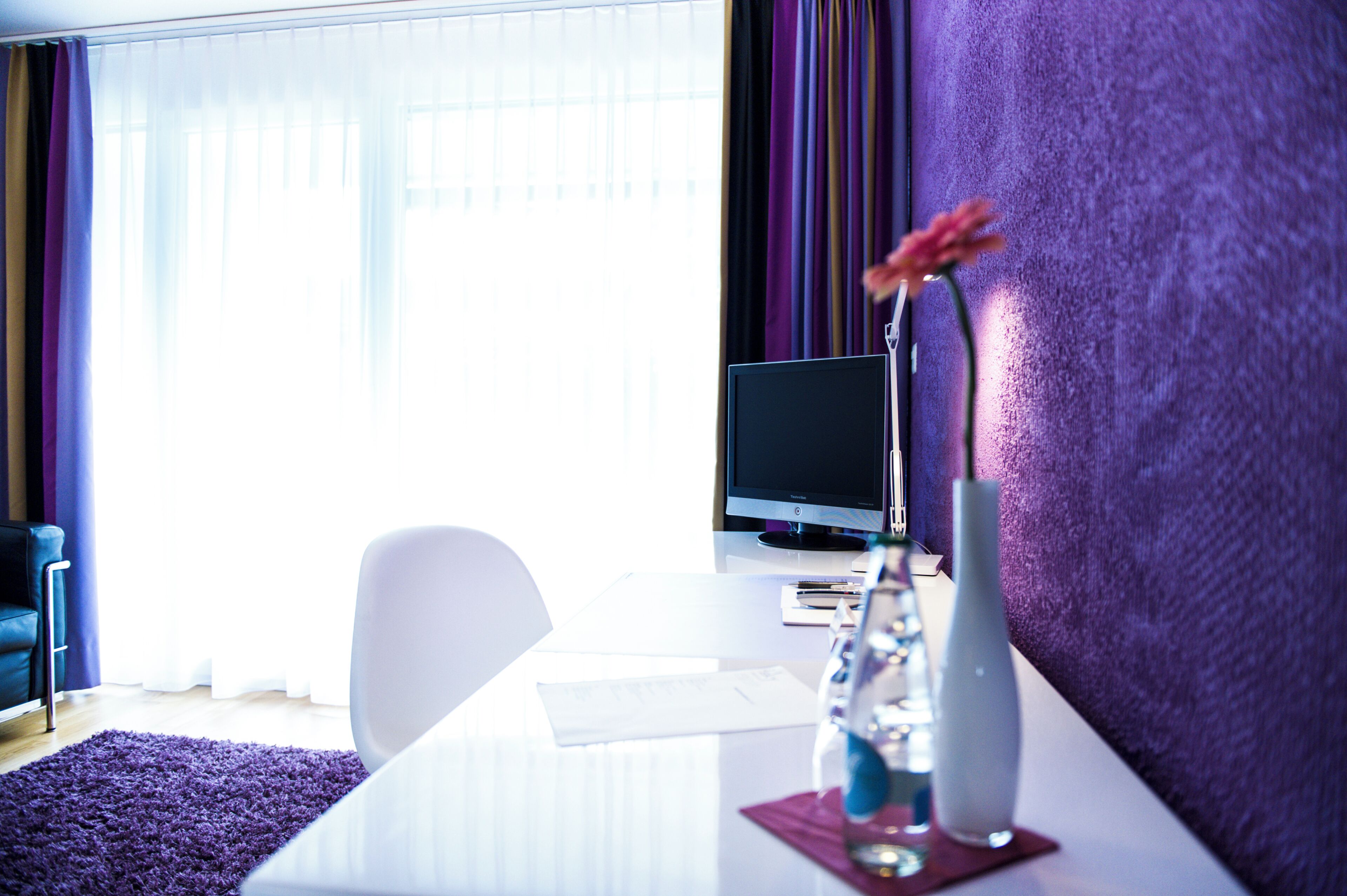 Une chambre d’hôtel équipée d’un bureau, d’un ordinateur et d’un vase avec une fleur.