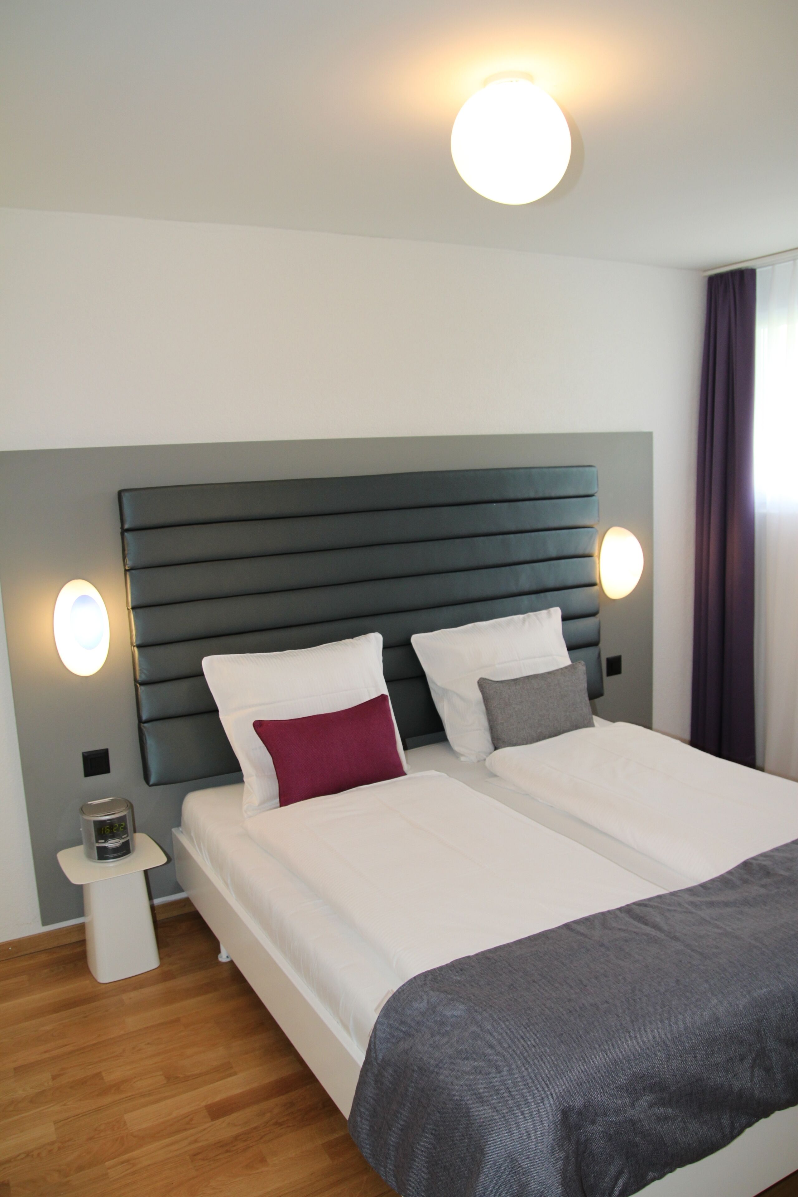 A double bed with a grey headboard and two bedside tables, each with a wall-mounted lamp.