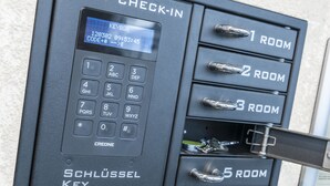 A self-check-in kiosk with a keypad and a digital display. It has numbered keys for room selection and a metal handle for opening a drawer. - Sky Motel (Oberriet)