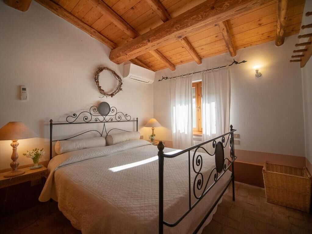 Quarto com teto de madeira, estrutura de cama de metal, duas mesas de cabeceira com abajures, uma planta na cabeceira e uma cesta de vime.