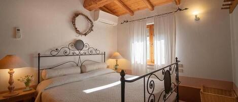 Quarto com teto de madeira, estrutura de cama de metal, duas mesas de cabeceira com abajures, uma planta na cabeceira e uma cesta de vime.