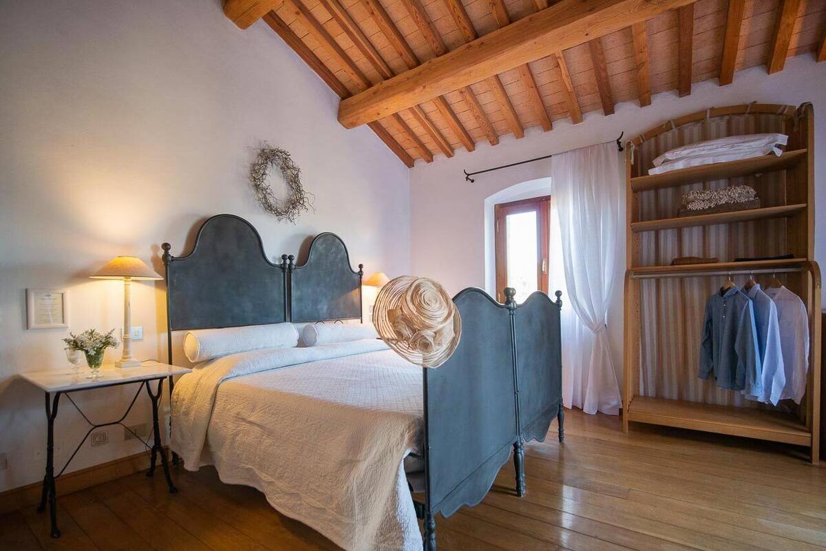 A bedroom with a bed, bedside table, lamp, and a wooden wardrobe with clothes.