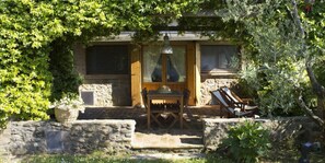 A stone building with a wooden door and windows, a table with chairs, and a stone wall with a basket of flowers. - Podere Le Mezzelune (Bibbona)