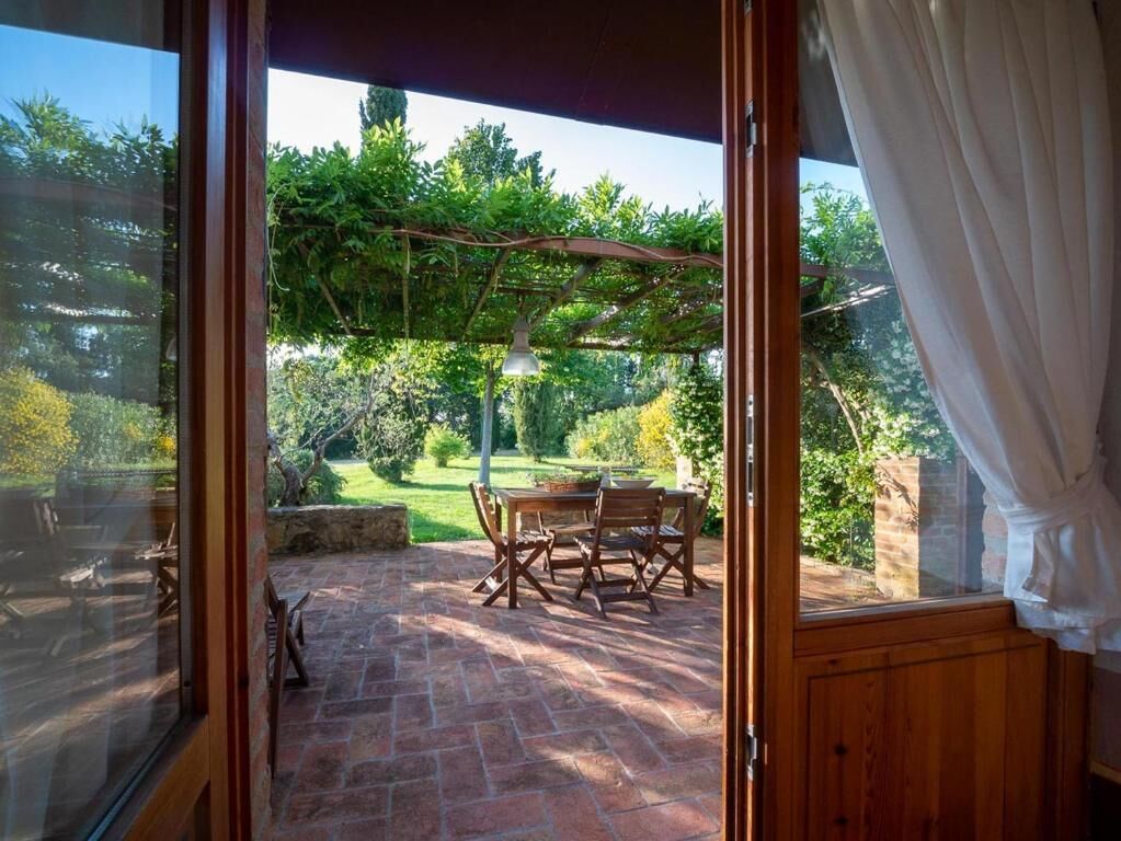 An open patio with a table and chairs, a hanging light fixture, and a view of a garden.