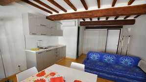 A modern kitchen with white cabinets and a wooden ceiling, a dining table with a floral tablecloth, and a blue sofa in the living area. - Egidio studio apartment 2 (Florence)