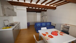 A compact kitchen with modern appliances, a dining area with a table set for two, and a blue patterned sofa in the background. - Egidio studio apartment 2 (Florence)