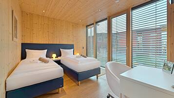 A modern hotel room with two beds, a desk, and a large window with blinds.