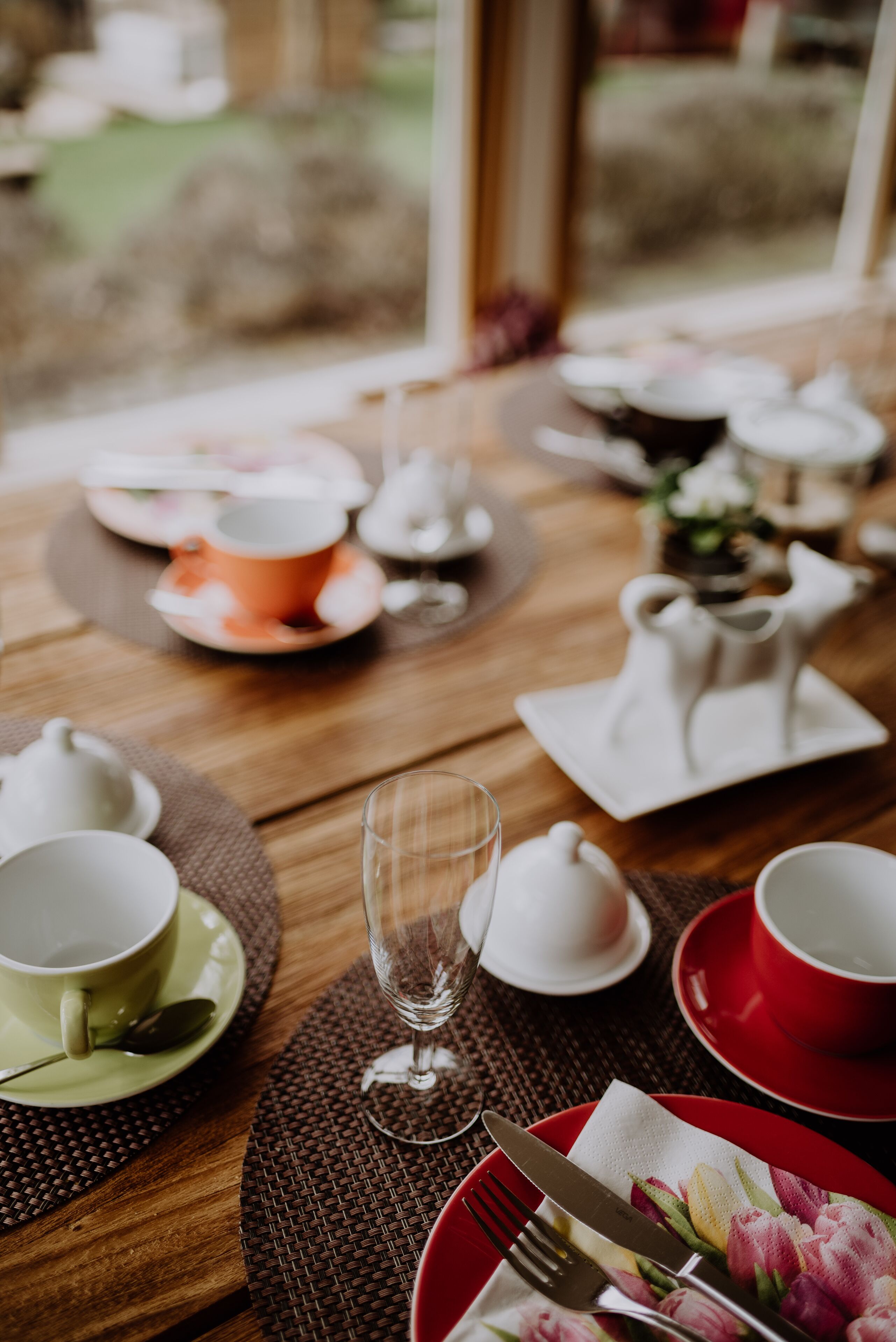 A dining table set with various dishes and utensils, including cups, plates, and a glass.