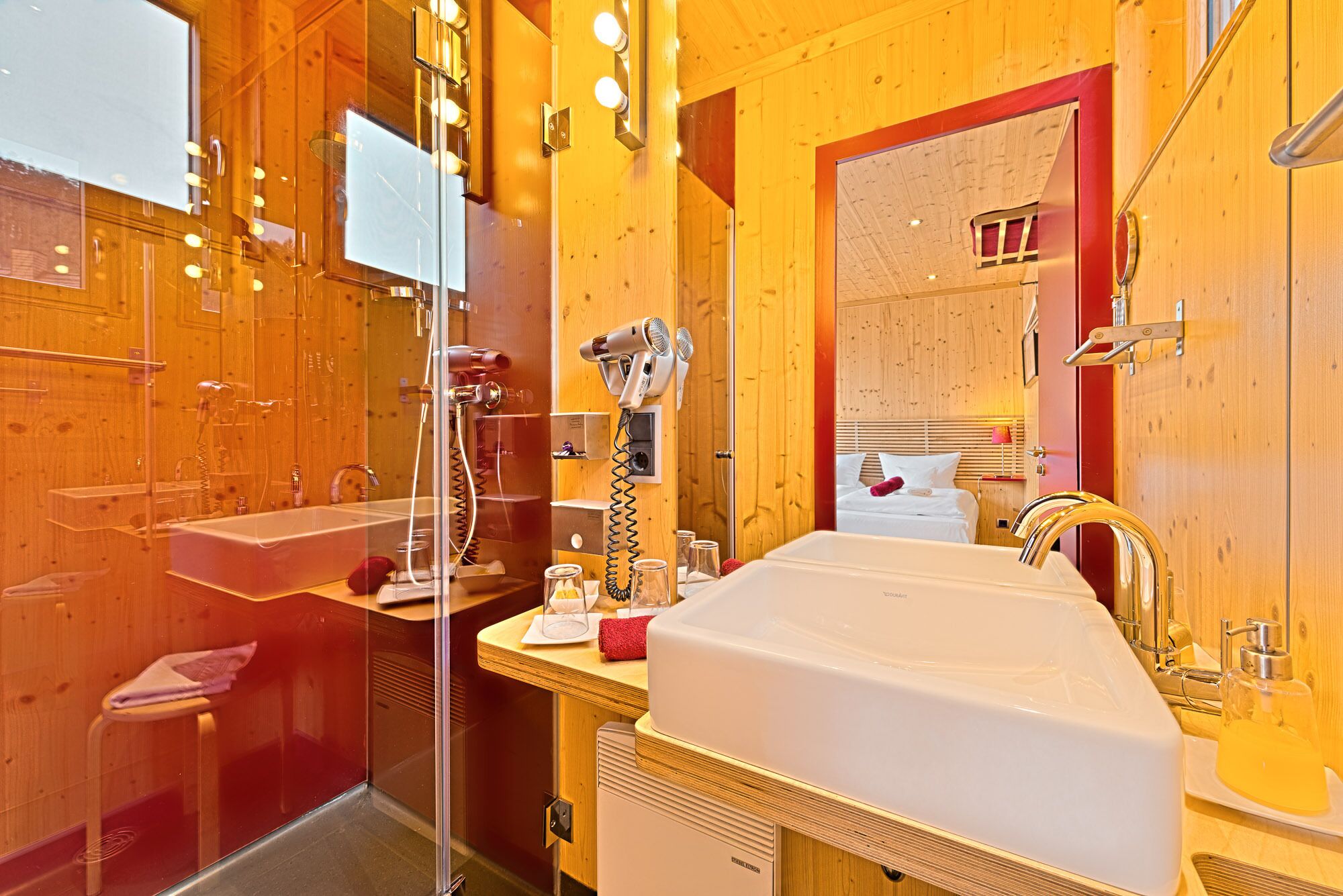 A modern bathroom with a glass-enclosed shower, a white sink, and a mirror with a red frame.