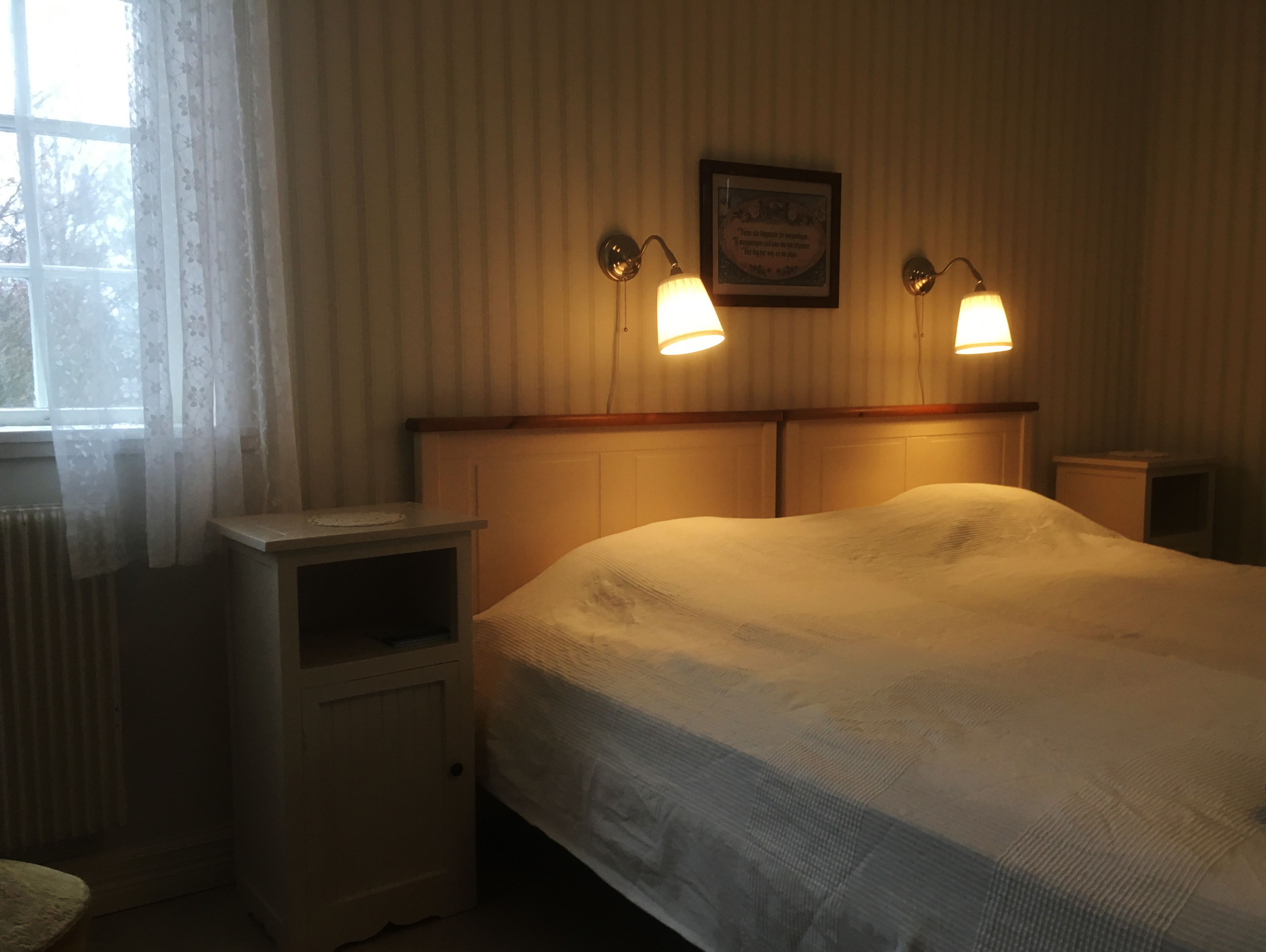 A bedroom with a bed, bedside tables, a window with curtains, and wall-mounted lamps.