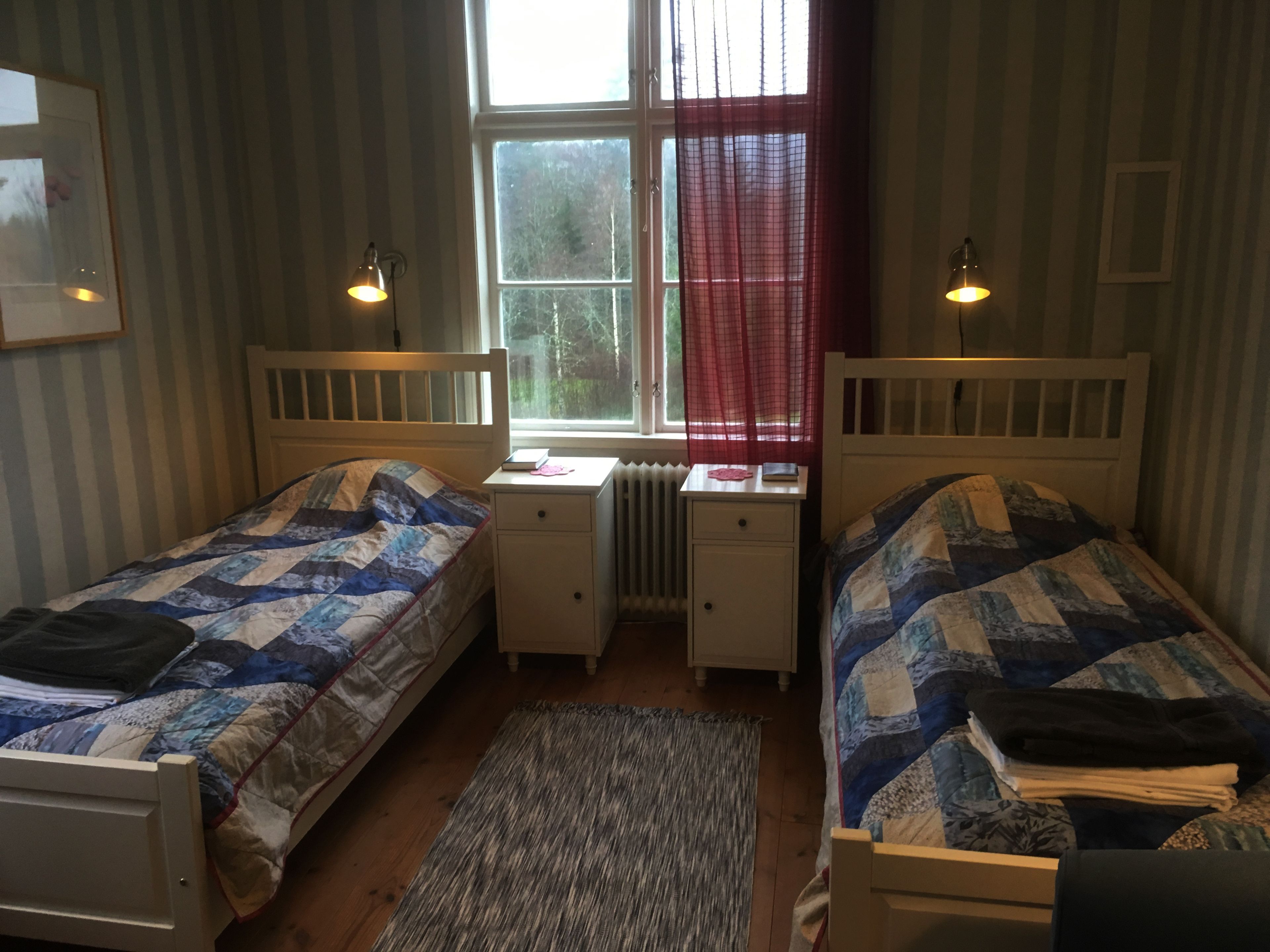 Un dormitorio doble con dos camas individuales, un escritorio pequeño y una ventana con cortinas.
