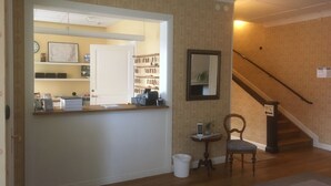 Un espace d’accueil comprenant un comptoir, un porte-manteau, une petite table avec une plante, une chaise et un escalier avec une indication signalant la direction des toilettes.