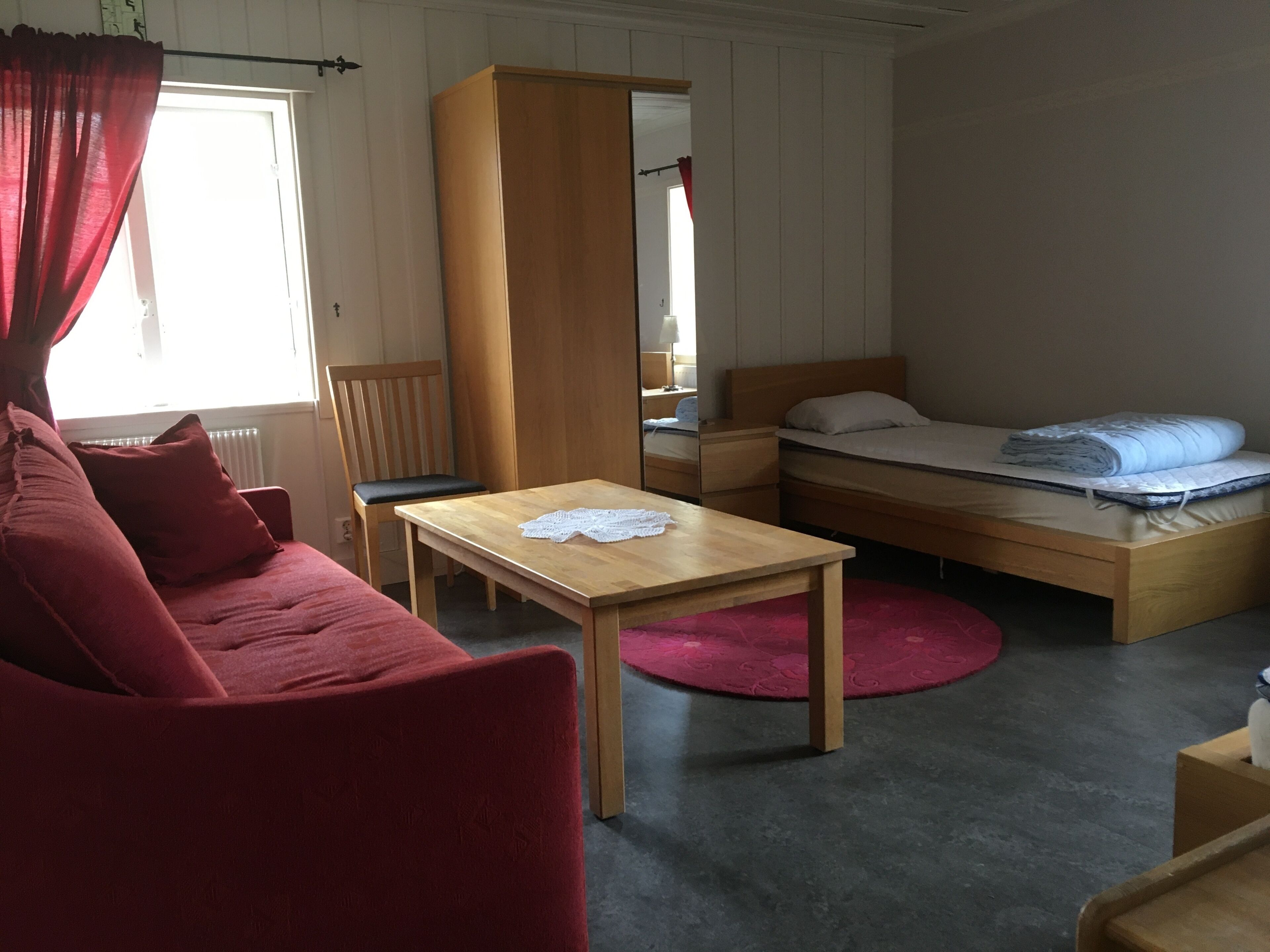 A cozy room with a wooden bed, a red sofa, a wooden table, and a red rug.