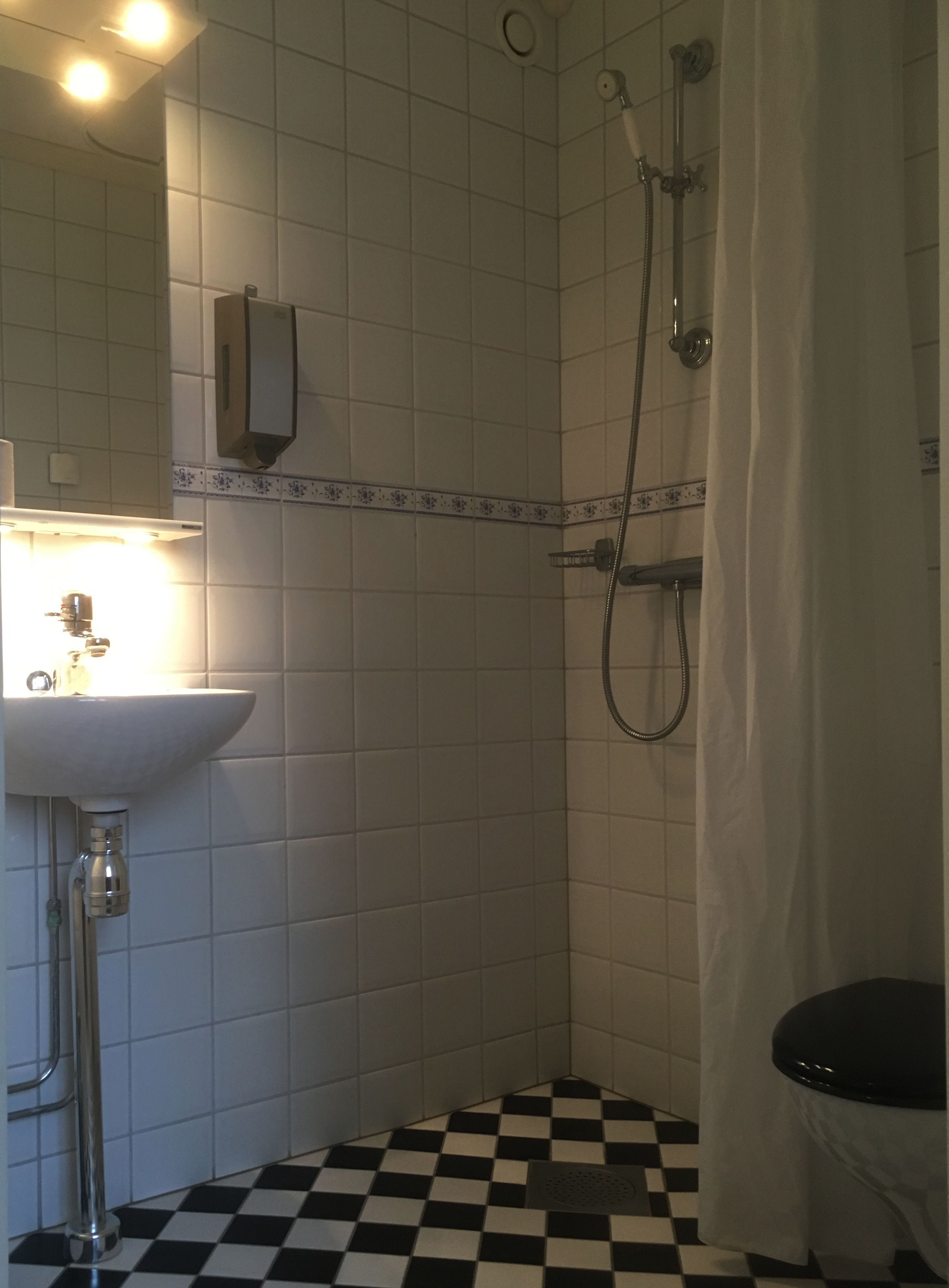 Ett badrum med ett vitt handfat, en dusch med duschdraperi och ett svart- och vitrutigt golv.