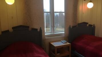 A room with two beds, a small table, a window, and wall-mounted lights.