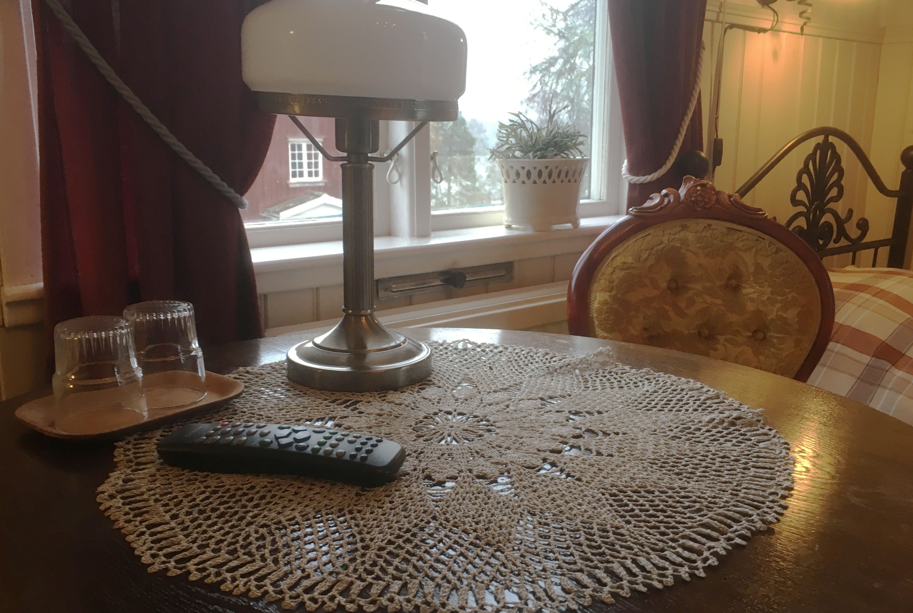A table with a doily, a remote control, and two glasses on a tray.