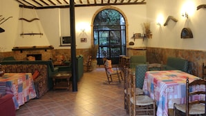 A cozy dining area with wooden chairs and tables, a fireplace, and a large arched window providing natural light. - Casa Rural La Fabrica De Nacelrio (Cazorla)