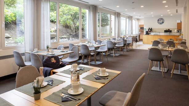 A dining area with tables, chairs, and a kitchen in the background. - Hotel Vetter (Nuertingen)