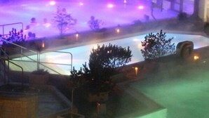 A swimming pool with a glass enclosure, surrounded by trees and a stone wall. - Hotel Vetter (Nuertingen)