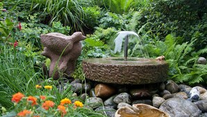 A garden with a stone fountain, surrounded by rocks and various plants. - Hotel Vetter (Nuertingen)