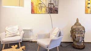 A modern room with two white armchairs, a wooden coffee table, a Buddha statue, and abstract paintings on the wall. - Hotel Vetter (Nuertingen)