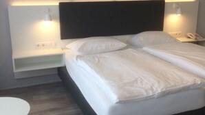 A neatly made bed with white linens, a dark headboard, and two bedside tables with lamps. - DAHL Hotel & Restaurant GmbH (Wachtberg)
