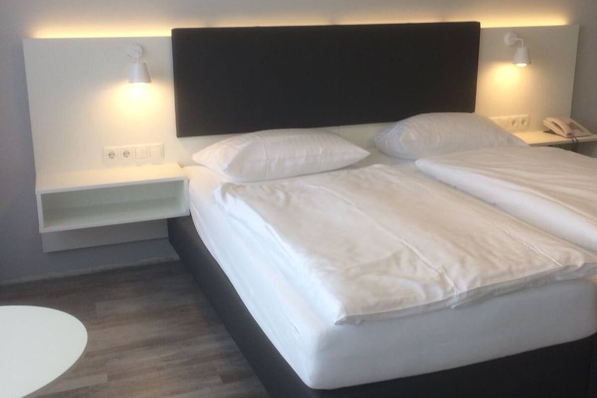 A neatly made bed with white linens, a dark headboard, and two bedside tables with lamps.