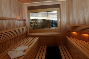 A sauna with wooden benches and a window providing a view of buildings and trees. - DAHL Hotel & Restaurant GmbH (Wachtberg)