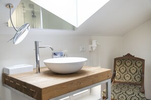 A modern bathroom with a skylight, a wooden vanity, a white sink, and a vintage chair. - Villa Bergmann Suites Meran (Merano)