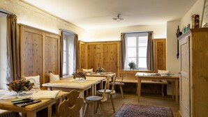 Une pièce chaleureuse, meublée de meubles en bois, avec une table à manger, des chaises, un banc et une grande fenêtre agrémentée de rideaux.