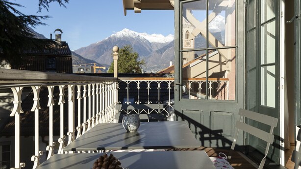 Un balcon avec une table, une chaise et une vue sur des montagnes enneigées.