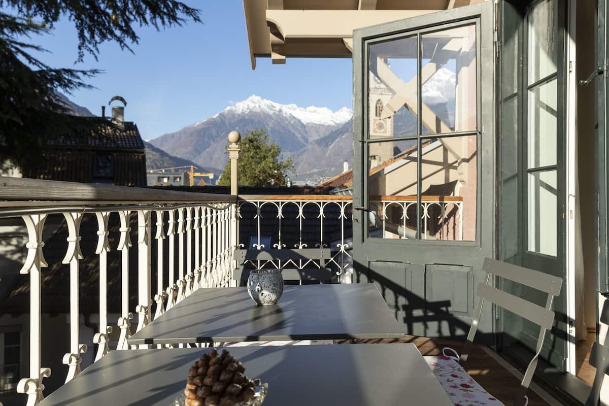 A balcony with a table, a chair, and a view of snow-capped mountains.