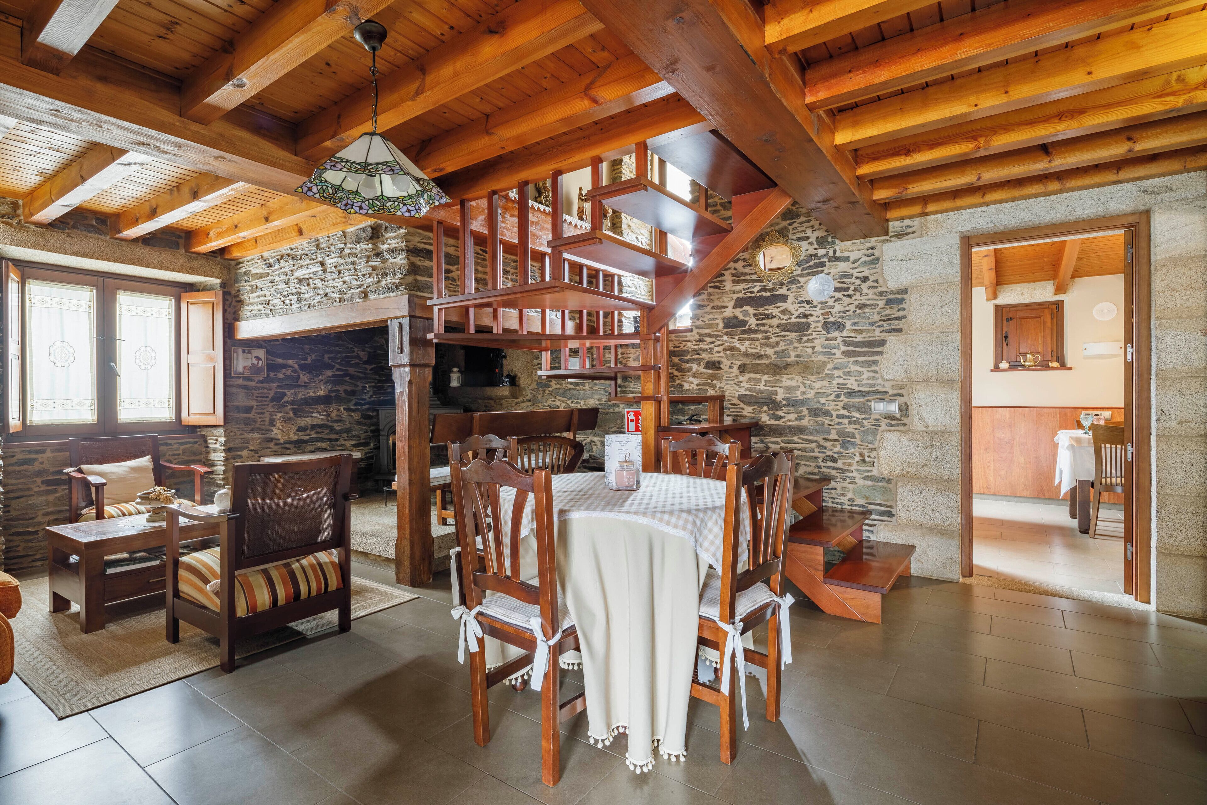 A rustic interior with a stone fireplace, wooden dining table, and chairs.