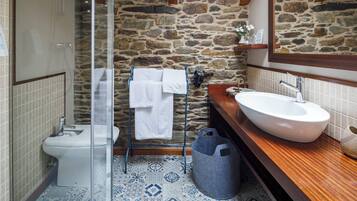 A bathroom with a stone wall, a white sink, a glass shower enclosure, and a patterned floor.