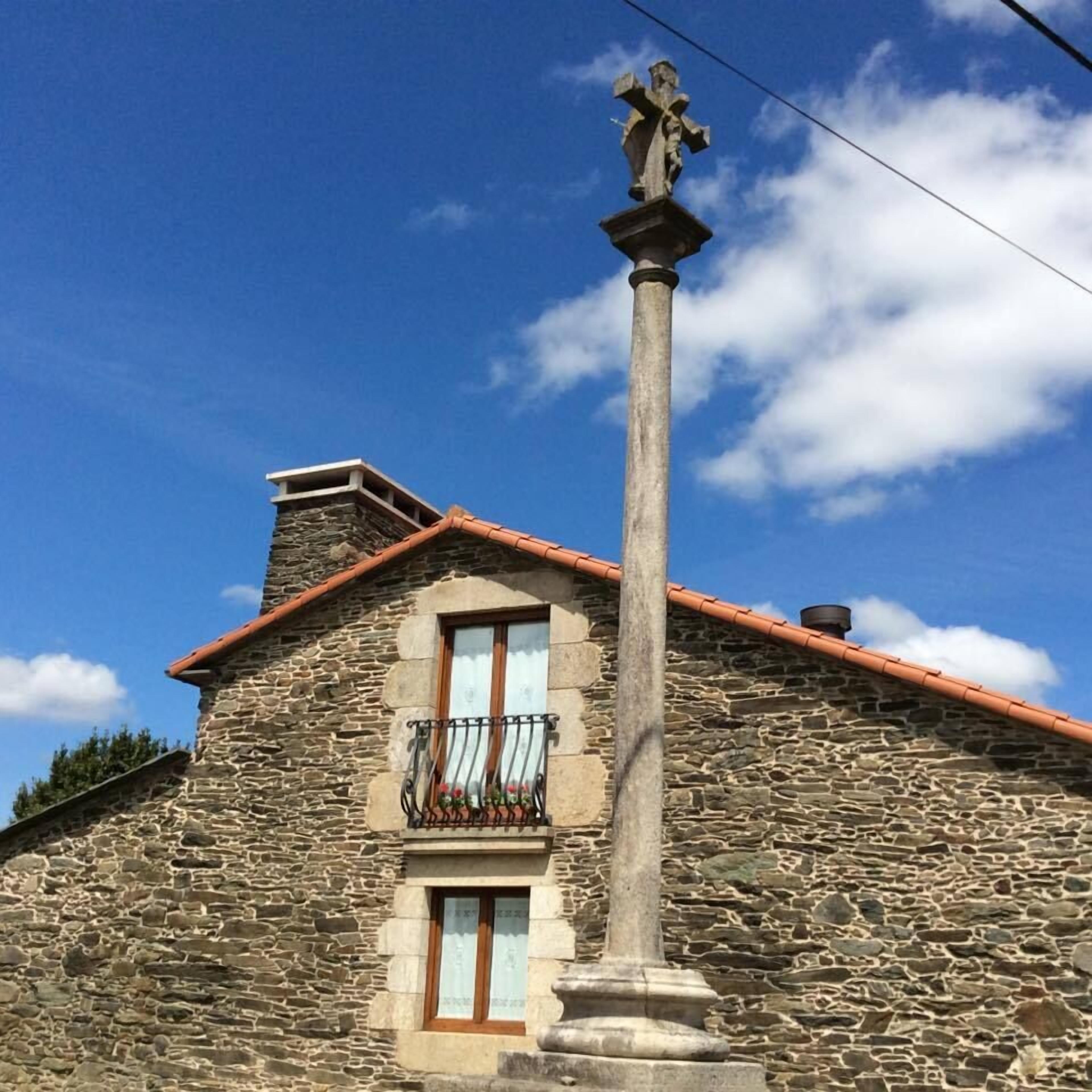 Un edificio de piedra con tejado de tejas, un balcón con barandilla de hierro forjado y una estatua sobre un pedestal.