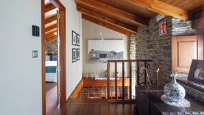 Una escalera de madera conduce a una zona superior con paredes de piedra y un colgante de luz.