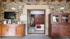Una habitación con paredes de piedra y techo de madera, un televisor montado en la pared, un armario de madera y una puerta que da a otra habitación.
