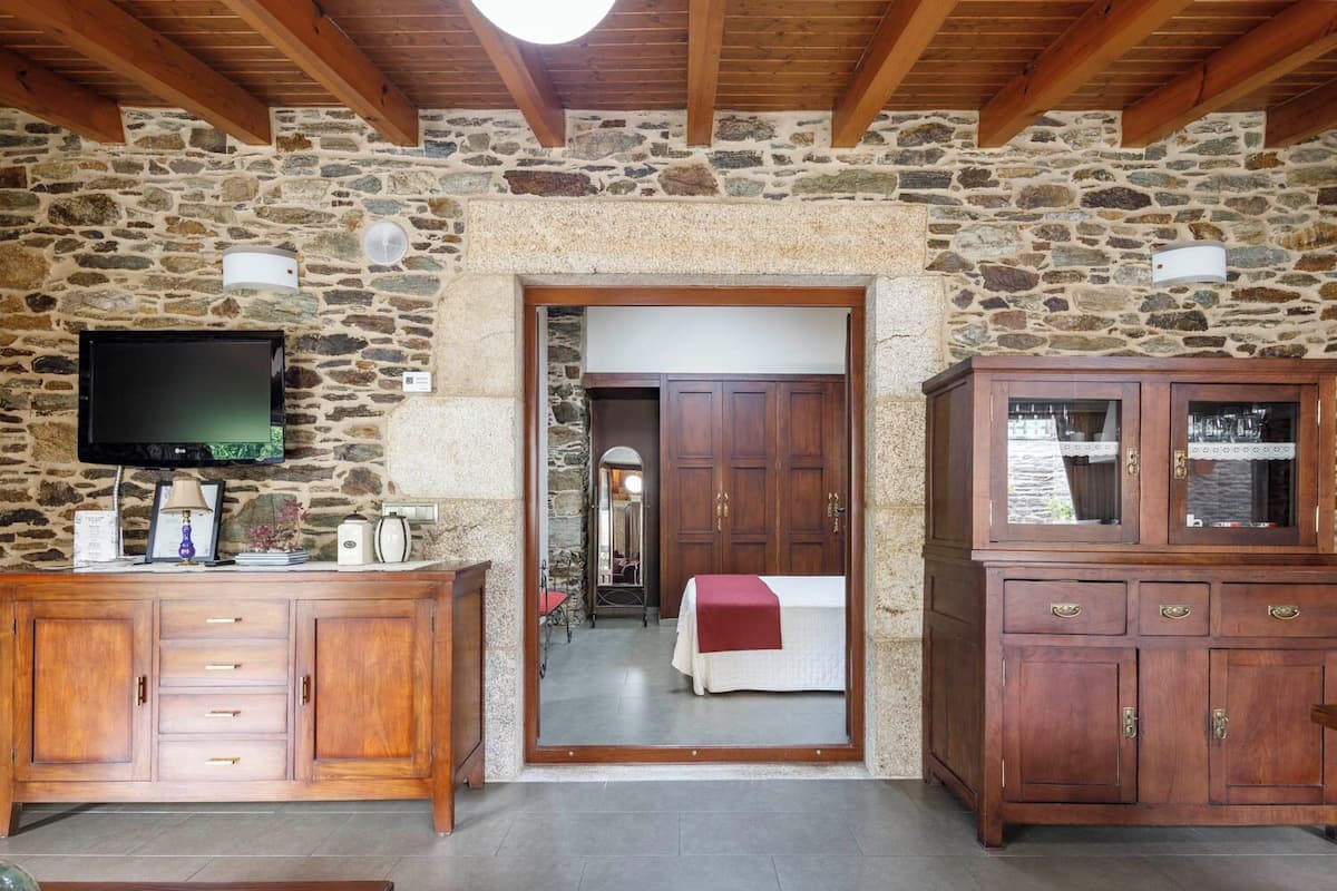 Une pièce aux murs de pierre et au plafond en bois, avec un téléviseur fixé au mur, un meuble en bois et une porte donnant sur une autre pièce.