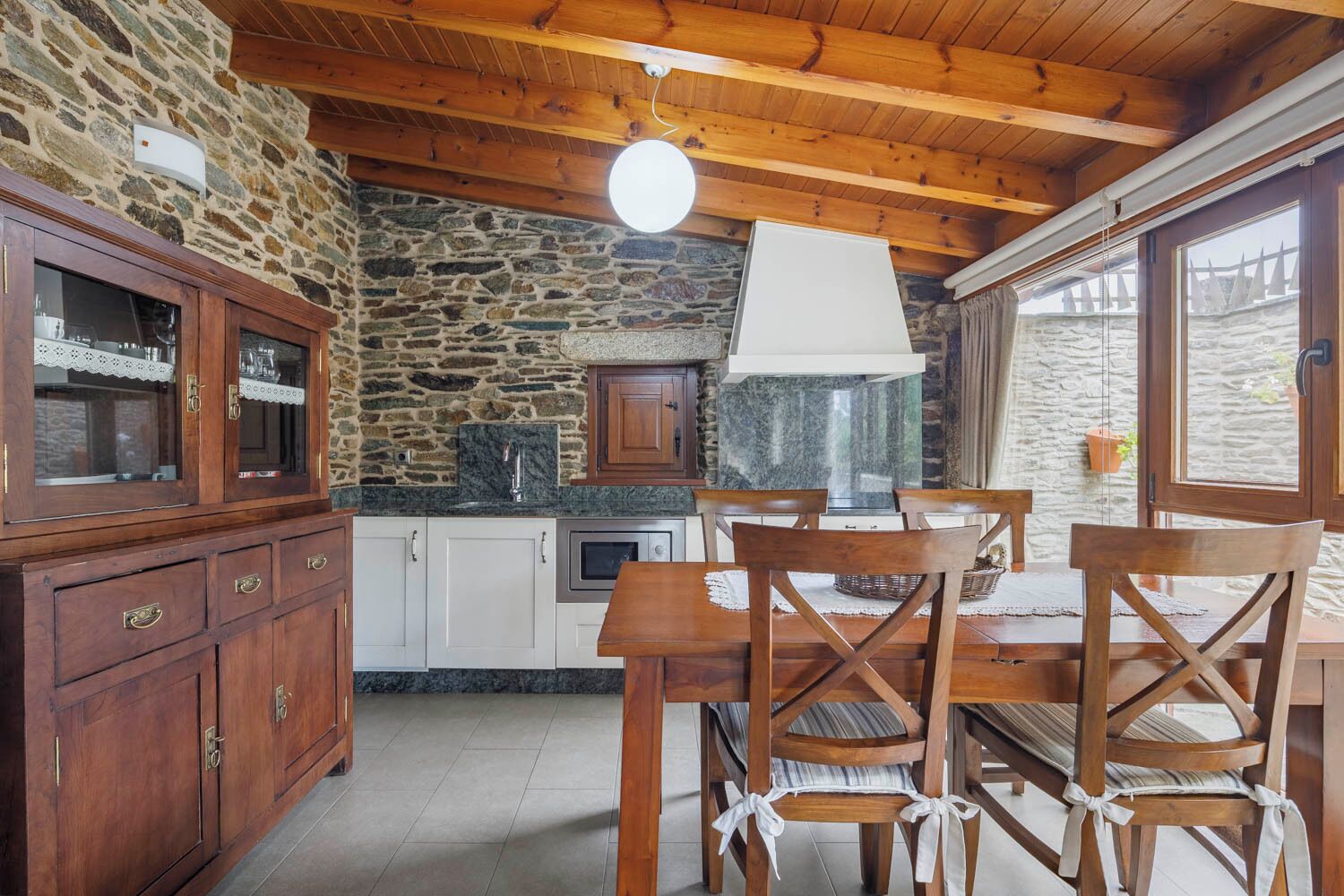 A rustic kitchen with stone walls, wooden cabinets, and a dining area with a table and chairs.