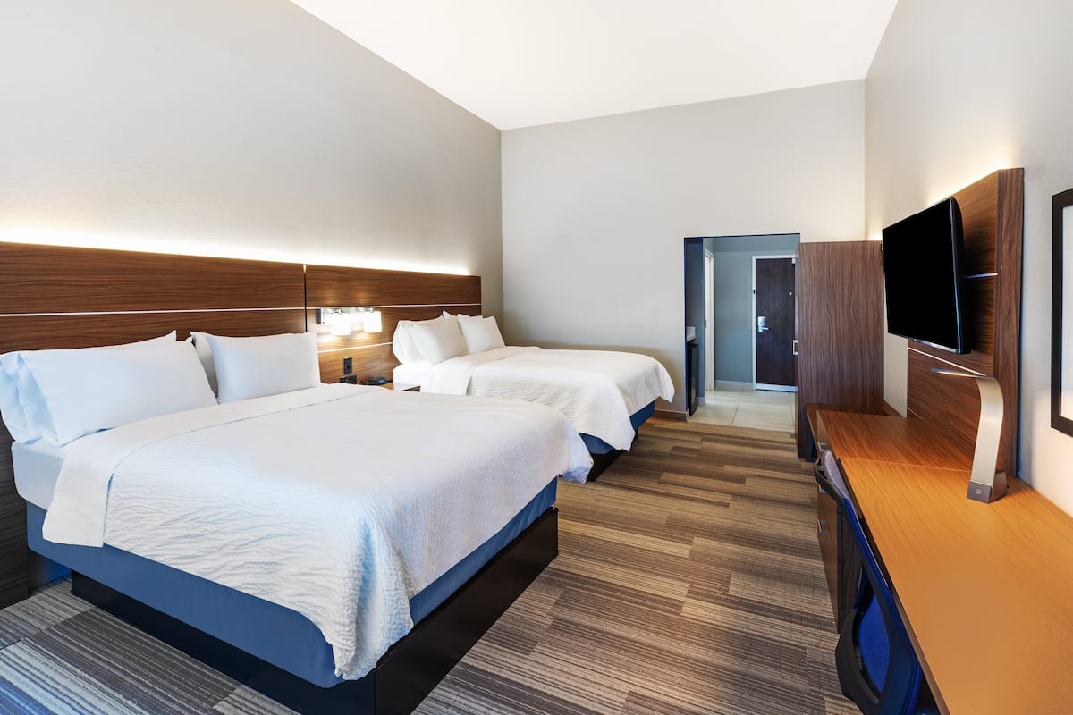 A hotel room with two beds, a flat-screen TV, a desk, and a door leading to another room.
