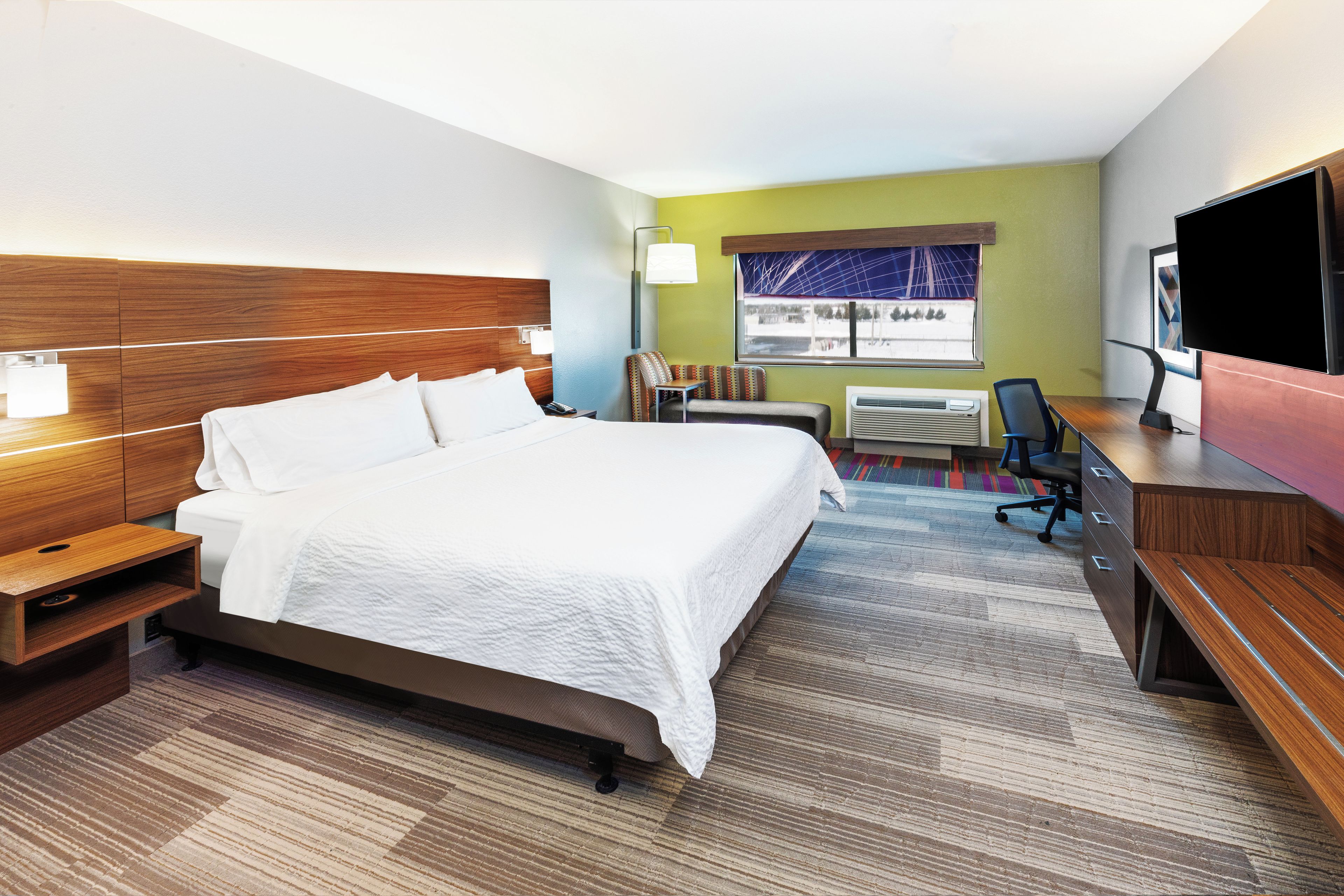 A hotel room with a large bed, a desk, a chair, a television, and a window with a view.