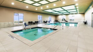 Piscina interior com várias pistas de natação, claraboia e área de estar com cadeiras e mesa.