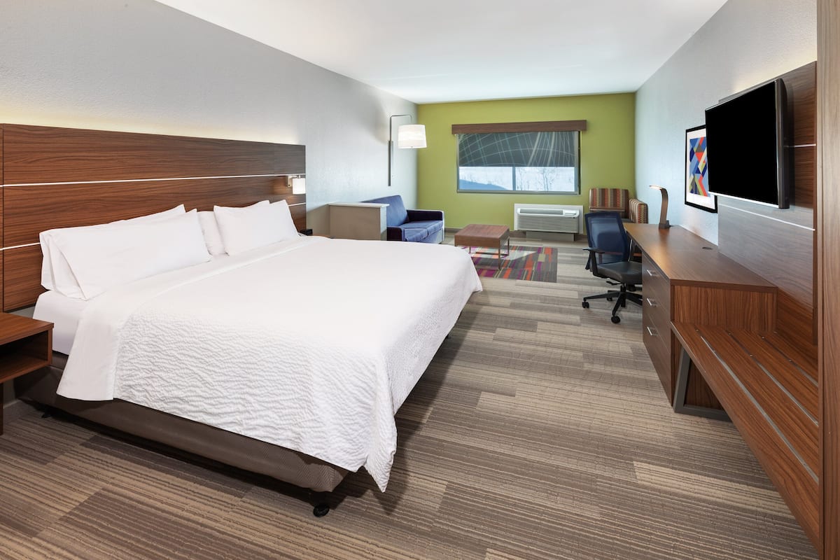 A hotel room with a large bed, a desk, a chair, a TV, and a window.