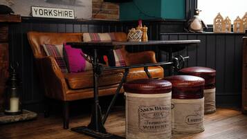 A cozy room with a leather sofa, a vintage table, and three wooden barrels labeled with whiskey brands.