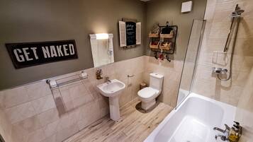 A modern bathroom with a toilet, sink, and bathtub. There is a 'GET NAKED' sign on the wall.