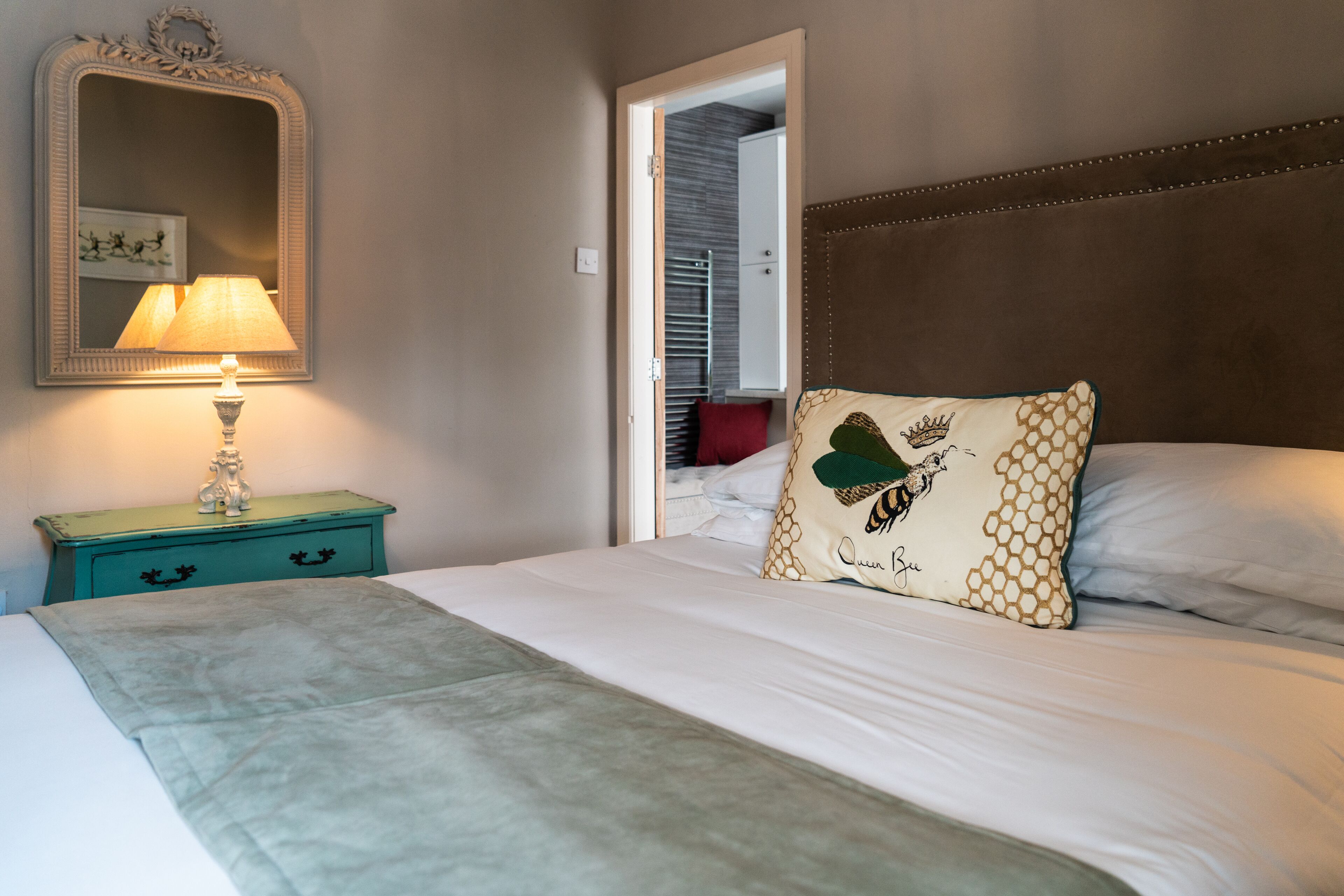 A bedroom with a bed, a nightstand with a lamp, a mirror, and a door leading to a closet.