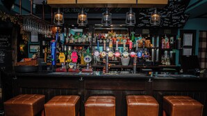 Un bar con varias grifos de cerveza, taburetes y una variedad de botellas y vasos.
