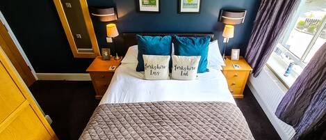 A hotel room with a bed, two bedside tables with lamps, a mirror, and framed pictures on the wall.