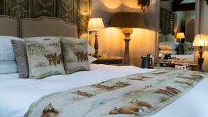 A neatly made bed with patterned pillows and a floral bedspread, a bedside table with lamps, and a mirror reflecting the room's decor. - Grantham Arms (York)